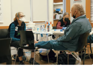 Masked healthcare workers assisting seated patient